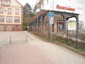 im Vordergrund gepflasterter Parkplatz. Hinten Bildmitte Rathaus, im Bild rechts Sparkasse.a