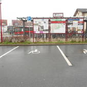Aufsicht auf die Parkplätze, weiße Bodenmarkierungen, im Hintergrund Gebäude des Bahnhofs sowie Wohnhäuser.