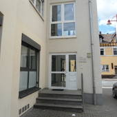 Im Bildhintergrund Rohrbacher Straße. Links vorne helles Gebäude mit vertikalen Fenstern. Mittig Glaseingangstür, davor 3 Stufen.