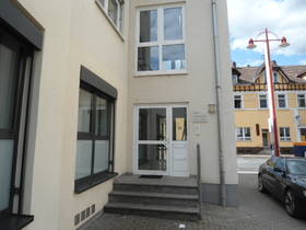 Im Bildhintergrund Rohrbacher Straße. Links vorne helles Gebäude mit vertikalen Fenstern. Mittig Glaseingangstür, davor 3 Stufen.