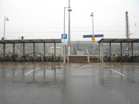 Aufsicht auf Parkplätze längs zum Gehweg vor dem Areal der S-Bahnhof-Gleise und Wartesteig.