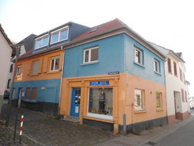 Halbseitenansicht des Hauses: EG rosa mit blauer Tür, davor 2 Stufen. 1. OG hellblau. Hausanteil links mit spiegelverkehrter Farbgebung. Daneben rechts weißes Haus. Vorne Teil des Gehwegs.